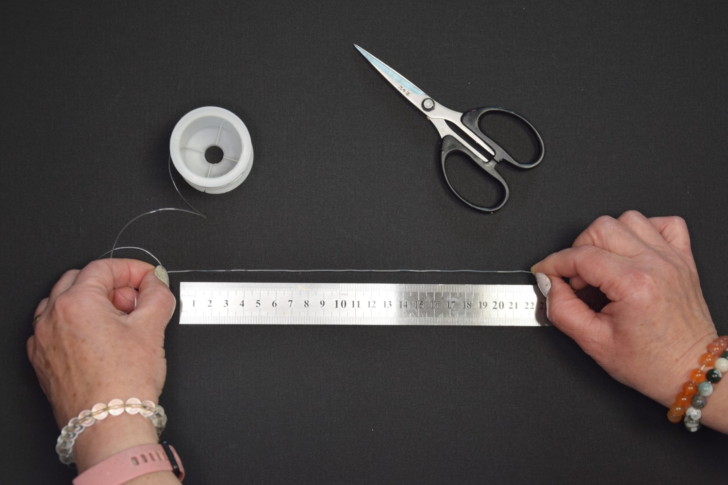 Žena vymeriava dĺžku nylonu pomocou kovového pravítka tak, aby bol dosť dlhý na vypletanie náramkov.